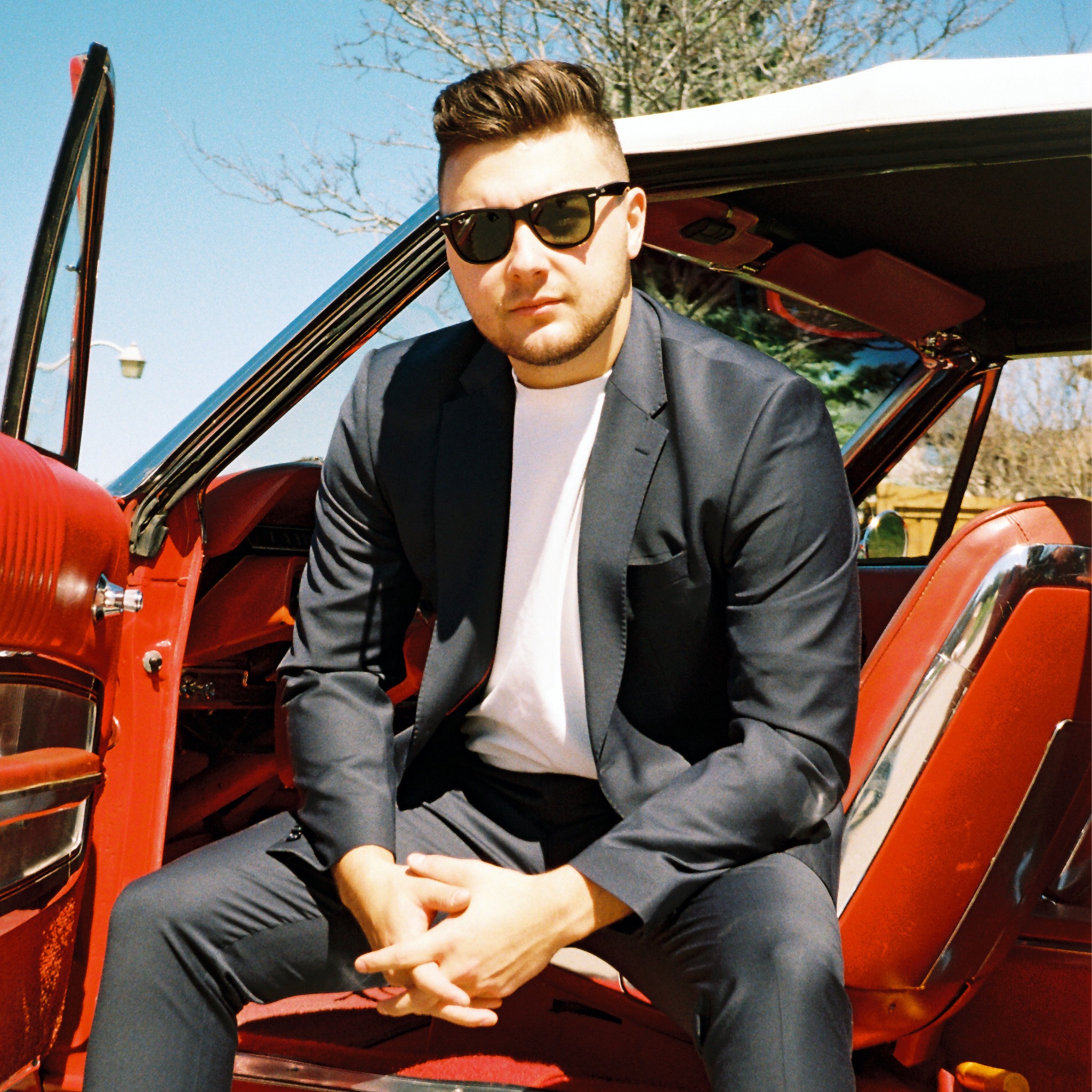 Nicholas Petrungaro seated beside a classic red car on the Start Again single cover